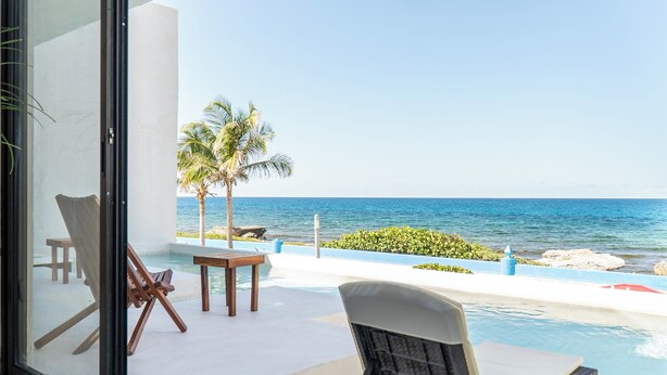 Un espace aménagé au bord de la piscine, avec des chaises longues, une table et une vue sur l’océan.