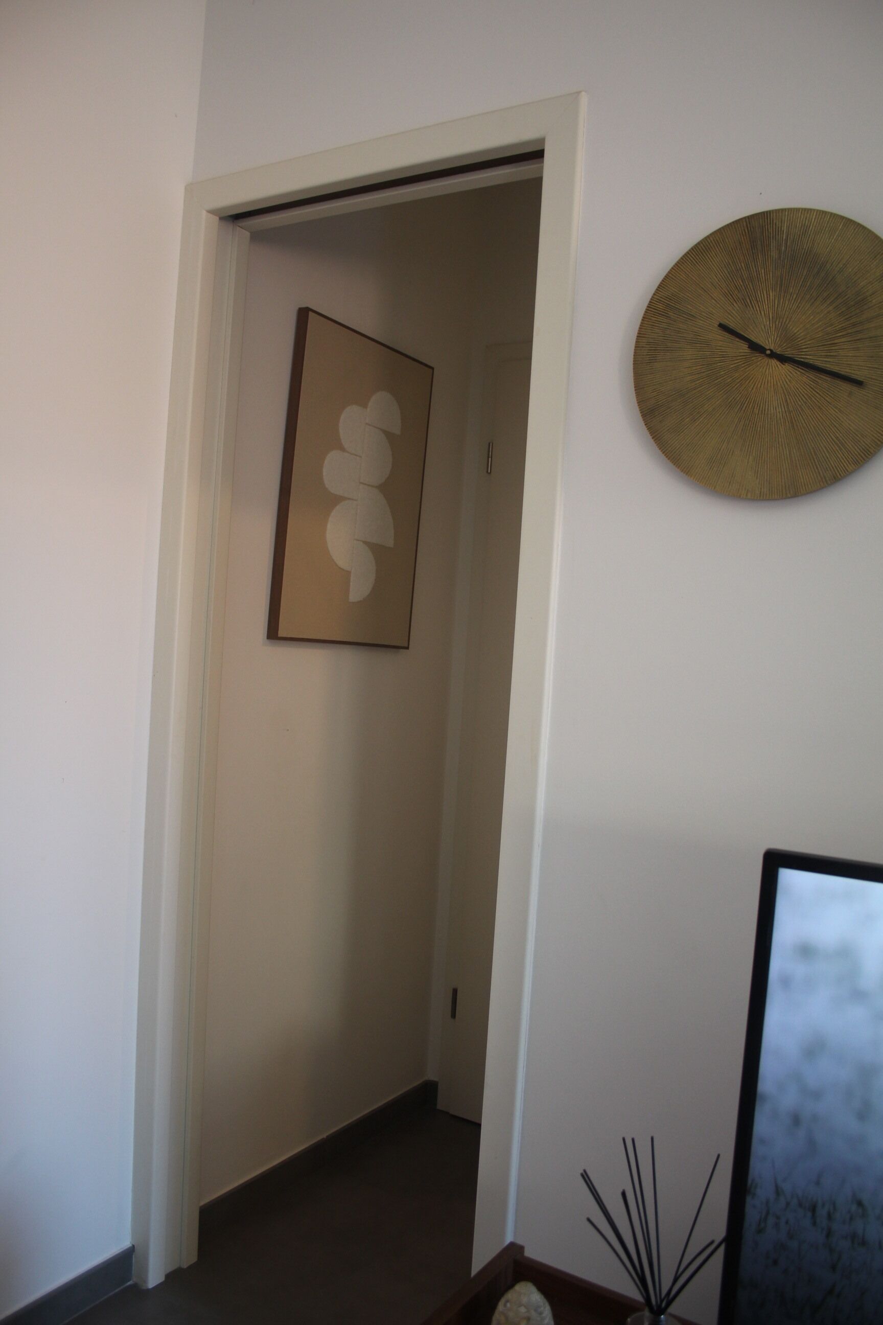 Un pasillo con una obra de arte abstracto enmarcada en la pared, un plato decorativo redondo y un pequeño florero con ramas.
