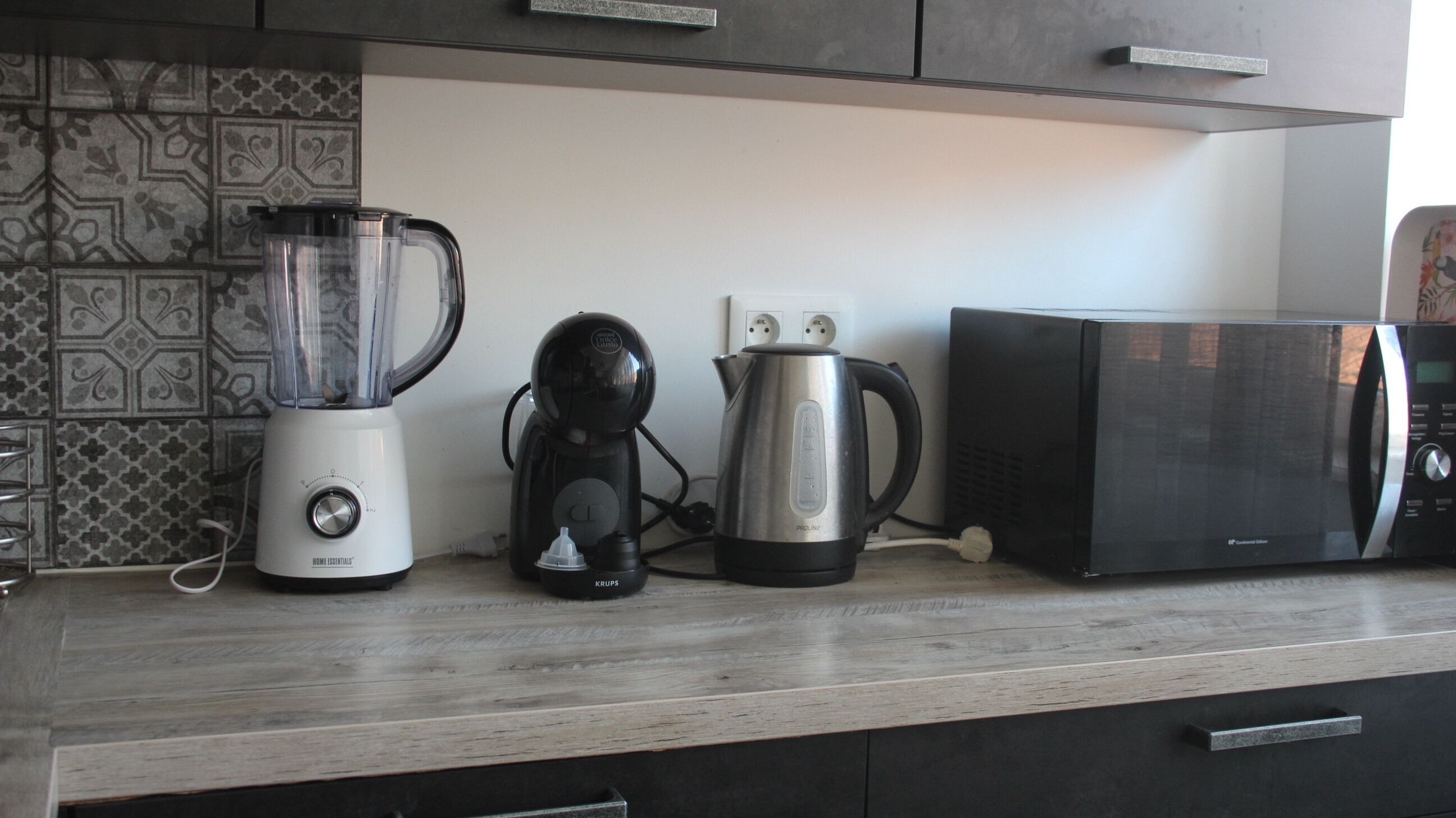 A kitchen counter with a blender, coffee maker, kettle, and microwave.
