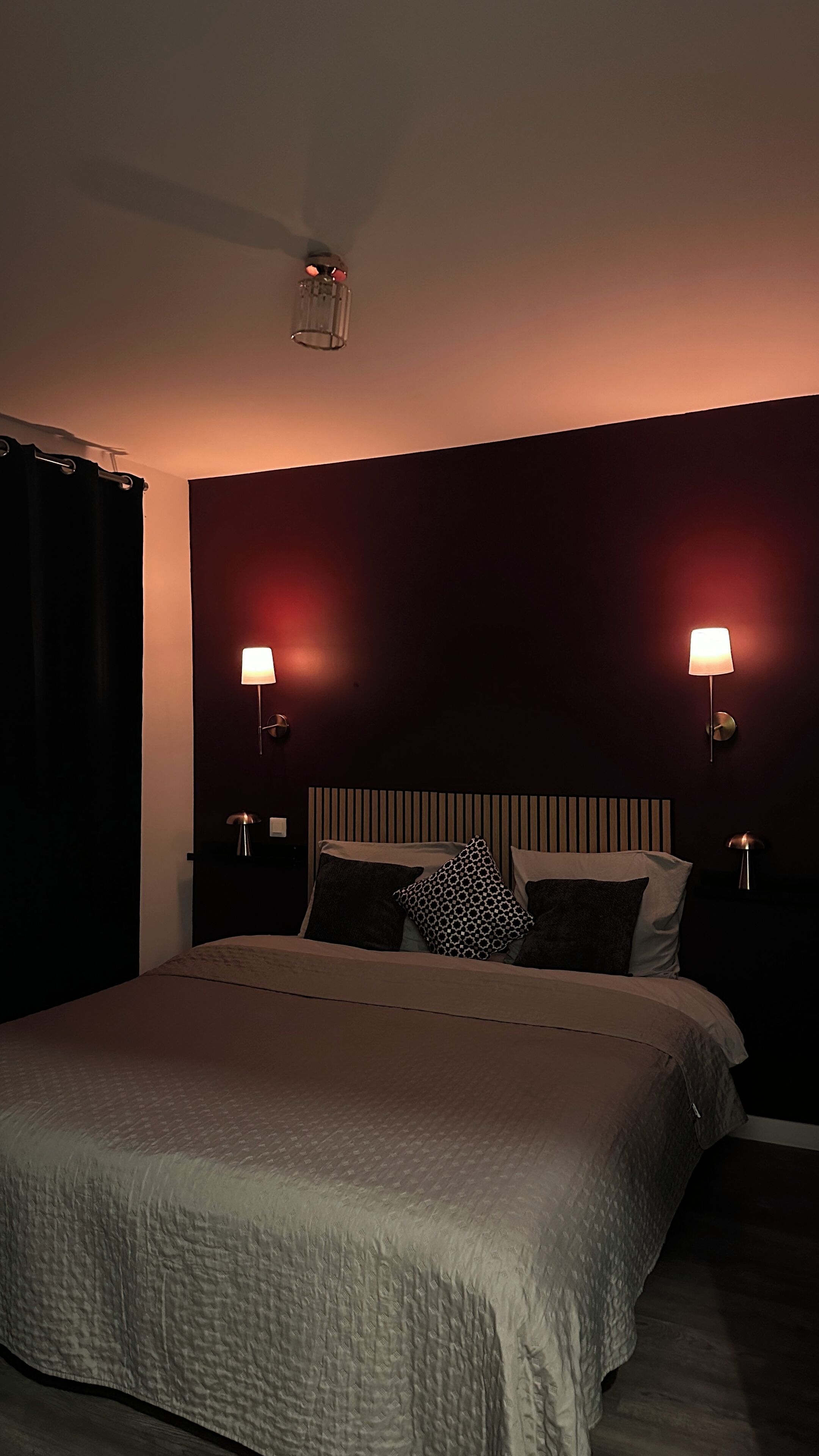 Une chambre à coucher avec un grand lit, deux lampes de chevet, un luminaire au plafond et des murs de couleur sombre.