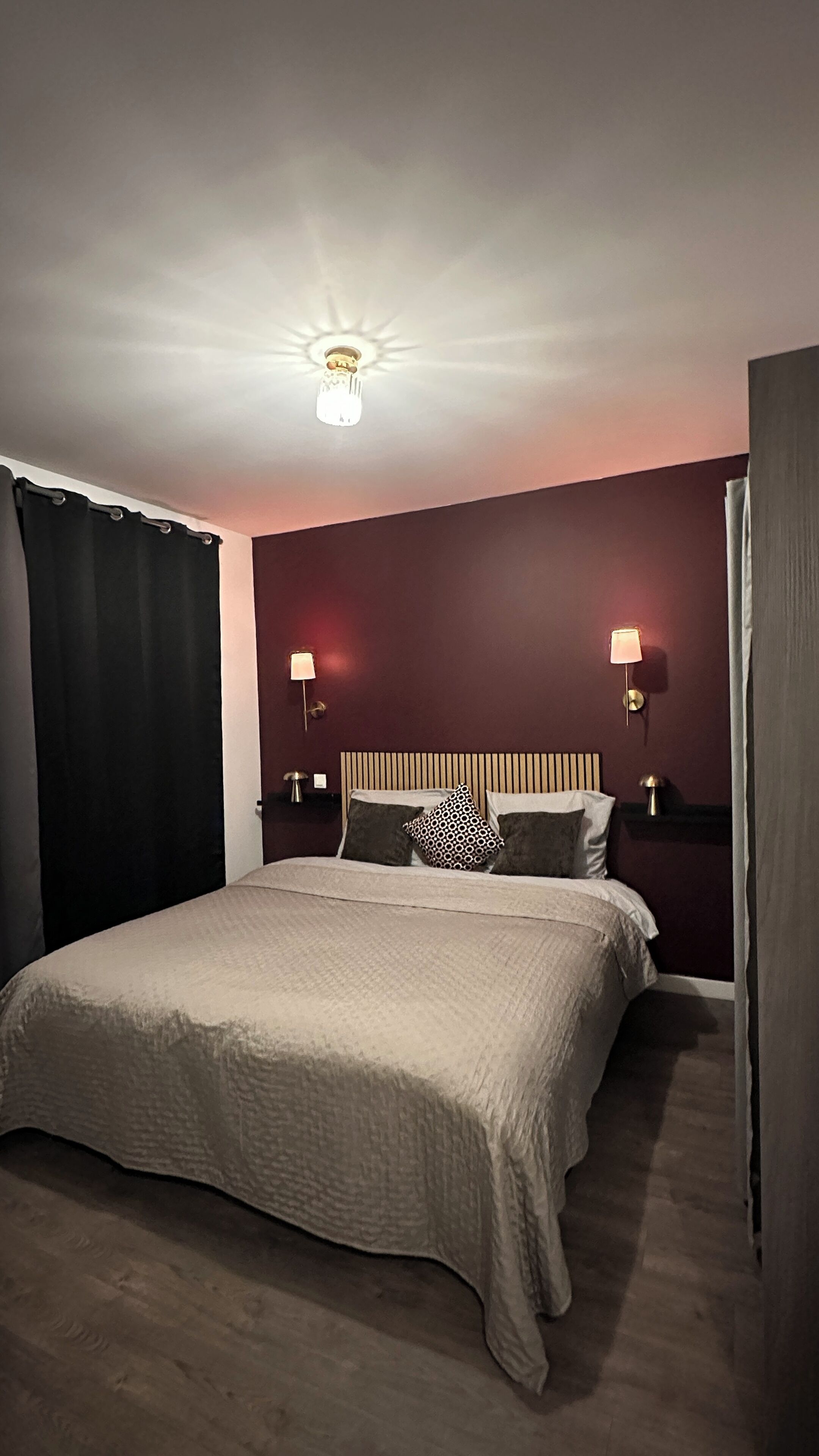 A bedroom with a large bed, two bedside lamps, a ceiling light, and dark curtains.