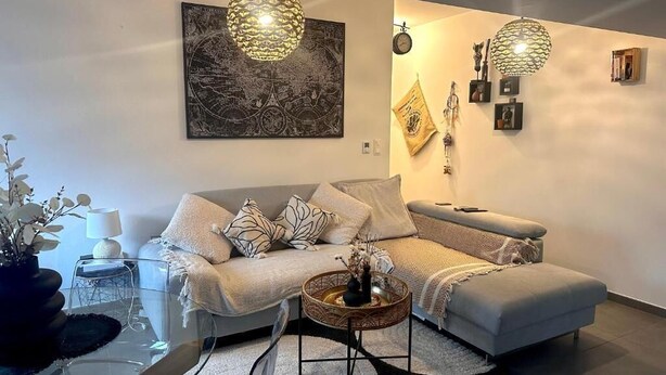 Una sala de estar moderna con un sofá gris, una mesa de centro de vidrio y detalles decorativos en la pared.