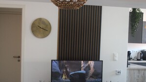 Un salón moderno con televisor, una lámpara de mimbre, un reloj y un mapa enmarcado de Lisboa.