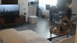 Una sala de estar moderna con sofá, televisión y comedor con mesa de vidrio y sillas.
