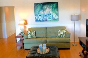 A living room with a sofa, a coffee table with candles, a painting, a lamp, and a television.