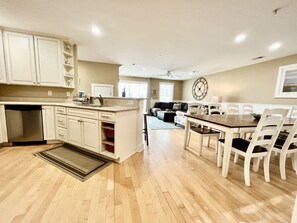 A kitchen with a dining area, wooden flooring, white cabinetry, and a clock on the wall. - Tybee Retreat Whole Building (Tybee Island)