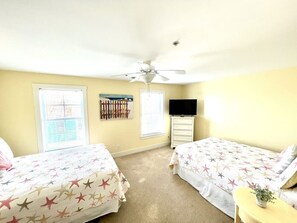 A bedroom with two beds, a ceiling fan, a TV, and a window with blinds.