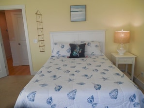 A bedroom with a bed, a bedside table, a lamp, and a wall-mounted shelf. - Tybee Retreat Whole Building (Tybee Island)