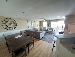 A spacious living area with a dining table, sofas, and a large wall clock.