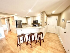 A kitchen with a central island, wooden stools, a refrigerator, a microwave, and a stove.