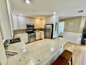 A kitchen with white cabinets, stainless steel appliances, a granite countertop, and a wooden bench. - Tybee Retreat Whole Building (Tybee Island)