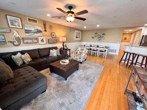 A living room with a sofa, ottoman, and chairs, a dining area with a table and chairs, and a kitchen with a refrigerator. - Tybee Retreat Whole Building (Tybee Island)