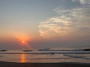 A beach scene with the sun setting over the ocean, waves approaching the shore, and a clear sky. - Tybee Retreat Whole Building (Tybee Island)