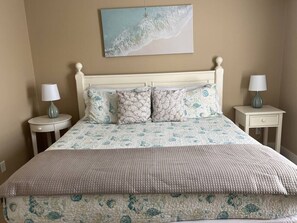 A bed with a patterned bedspread and pillows, flanked by two bedside tables with lamps. - Tybee Retreat Whole Building (Tybee Island)