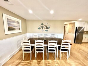 A dining area with a rectangular table and six chairs, a kitchen with white cabinets and a stainless steel refrigerator, and a wall-mounted decorative piece. - Tybee Retreat Whole Building (Tybee Island)