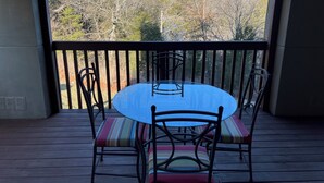A round table with chairs on a wooden deck, overlooking a forested area.