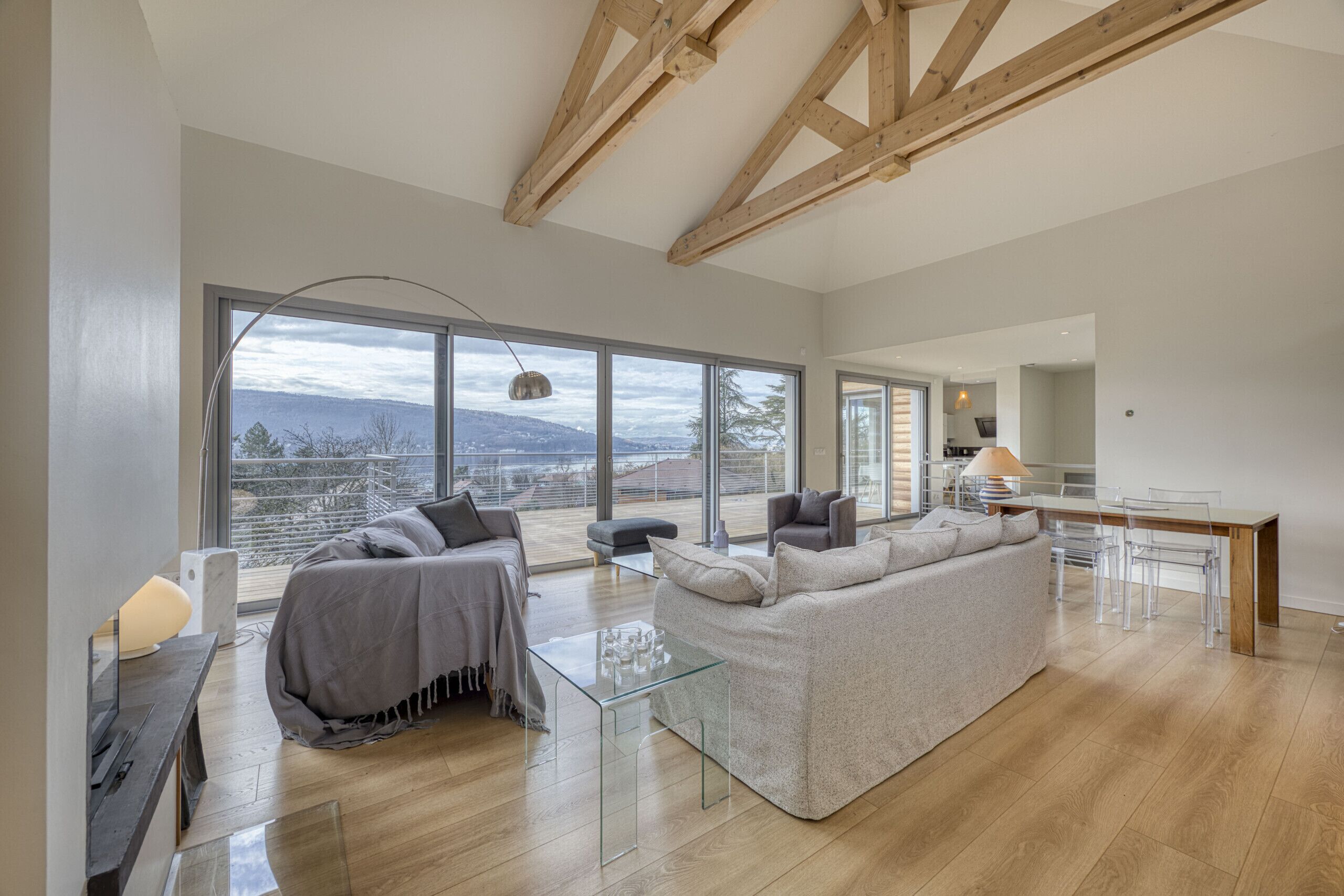 A spacious living area with a large window, a sofa, a glass coffee table, and a dining area with a table and chairs.