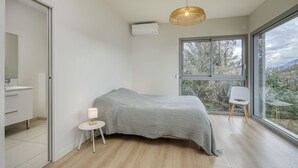 A modern bedroom with a bed, bedside table, lamp, and a large window offering a view of trees. - Wooden Villa 4* (Veyrier-du-Lac)