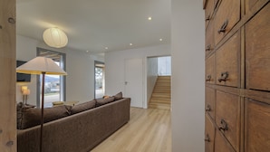 A modern interior with a sofa, a lamp, wooden cabinets, and a staircase. - Wooden Villa 4* (Veyrier-du-Lac)