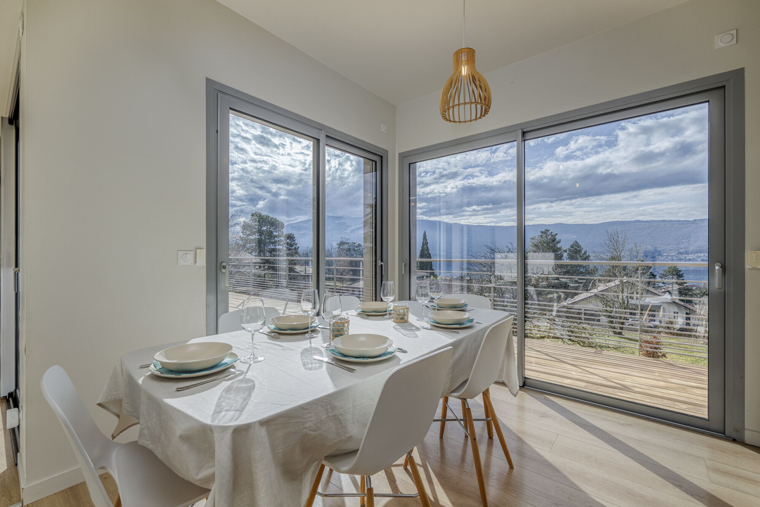 A dining area with a table set for four, large windows with a view, and a pendant light.