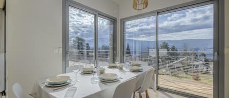 A dining area with a table set for four, large windows with a view, and a pendant light.