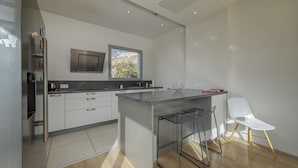 A modern kitchen with a central island, white cabinetry, and a window overlooking a mountainous landscape. - Wooden Villa 4* (Veyrier-du-Lac)