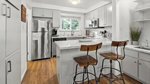A modern kitchen with white cabinetry, stainless steel appliances, a central island with bar stools, and a window providing natural light. - *Special* Lake~Hiking~Pool~Tahoe Townhome (Incline Village)