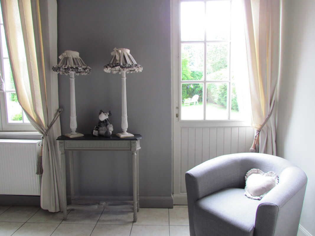 A room with a grey armchair, a white console table with two lamps, and a window with curtains.