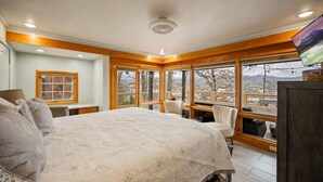 Ein Schlafzimmer mit einem großen Bett, Holzbalken, Blick auf die Stadt und einem großen Fenster.