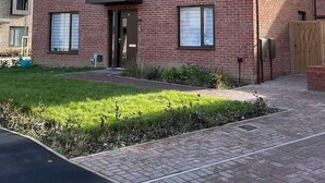 Un bâtiment à deux étages, construit en briques, avec un toit en pente, des panneaux solaires et un petit jardin à l’avant.