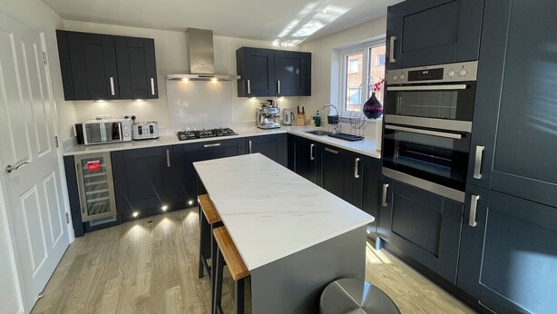 Une cuisine moderne avec des meubles de couleur sombre, un îlot central et des appareils électroménagers intégrés.