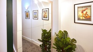 Un couloir avec des affiches encadrées accrochées au mur, une plante en pot et un luminaire.