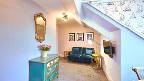 Un couloir avec une commode vert turquoise, un canapé vert foncé et un escalier dont les murs sont recouverts d’un papier peint représentant des voiliers.