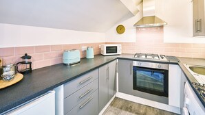Une cuisine compacte équipée d’une cuisinière à gaz, d’un four à micro-ondes, d’un grille-pain et d’une machine à café.