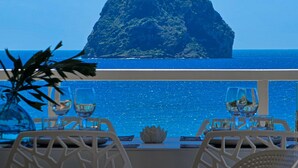 A table with two chairs and a vase of flowers, overlooking a clear blue sea and a rocky island. - Cézembre (Le Diamant)