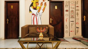A room with a glass coffee table, a brown sofa, and a wall mural of an Egyptian figure. - Nefertiti pyramids (Giza)