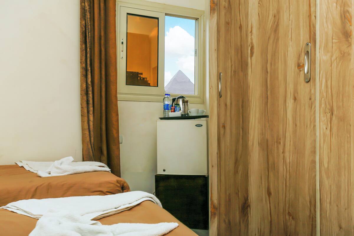 Una camera d'albergo con un letto, un angolo cottura, una finestra vista piramide e un armadio in legno.