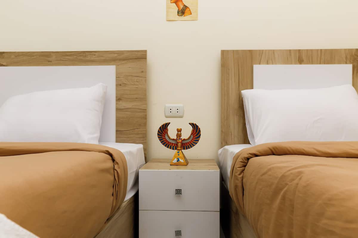 Camera d'albergo con due letti, ognuno con cuscini bianchi e biancheria marrone. Ogni letto ha una testiera in legno e un comodino con un oggetto decorativo posizionato tra i letti.