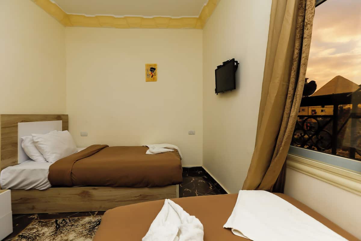 Camera d'albergo con due letti, una testiera in legno, una piccola TV a parete e una finestra con tende.