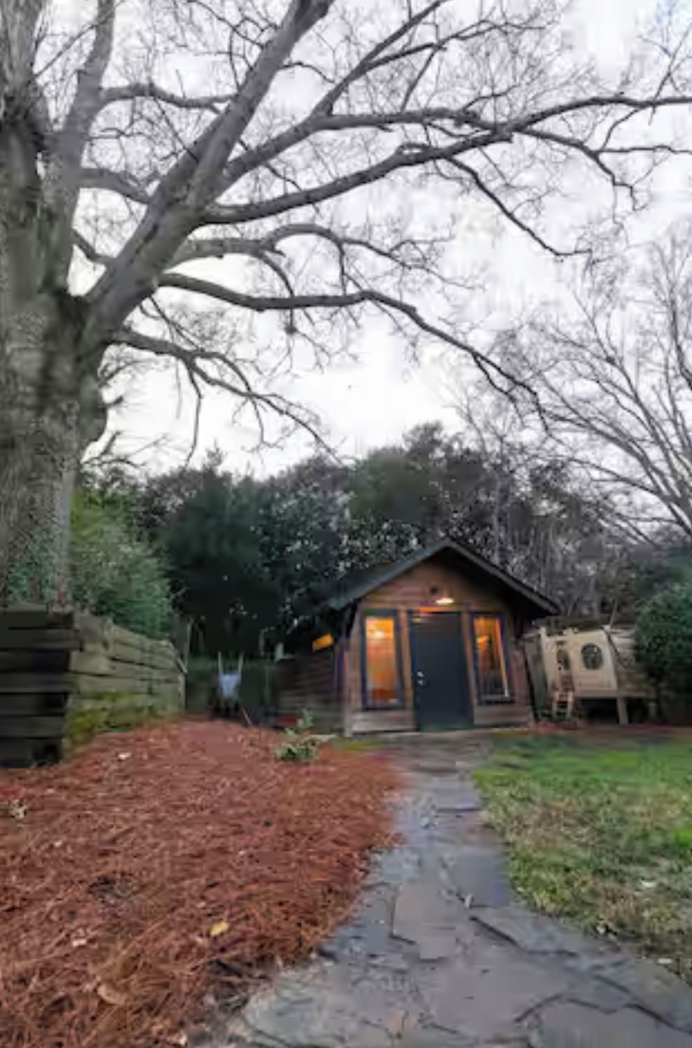 A rustic cabin with a stone pathway leading to the entrance, surrounded by trees and a wooden fence.