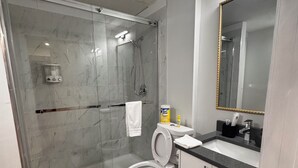 Un bagno moderno con cabina doccia in vetro, un WC bianco, un lavandino con specchio e una bottiglia di sapone per le mani.