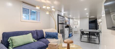 A modern living room with a sofa, a small round table, and a kitchen in the background.