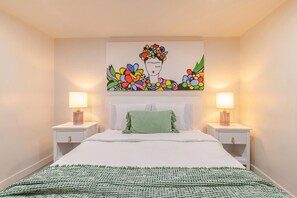 Ein Schlafzimmer mit einem Bett, zwei Nachttischen, einer Decke und einem farbenfrohen Blumenbild an der Wand.