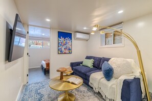 Ein modernes Wohnzimmer mit einer Couch, einem runden Goldtisch, einem an der Wand montierten Fernseher und einem farbenfrohen abstrakten Gemälde.