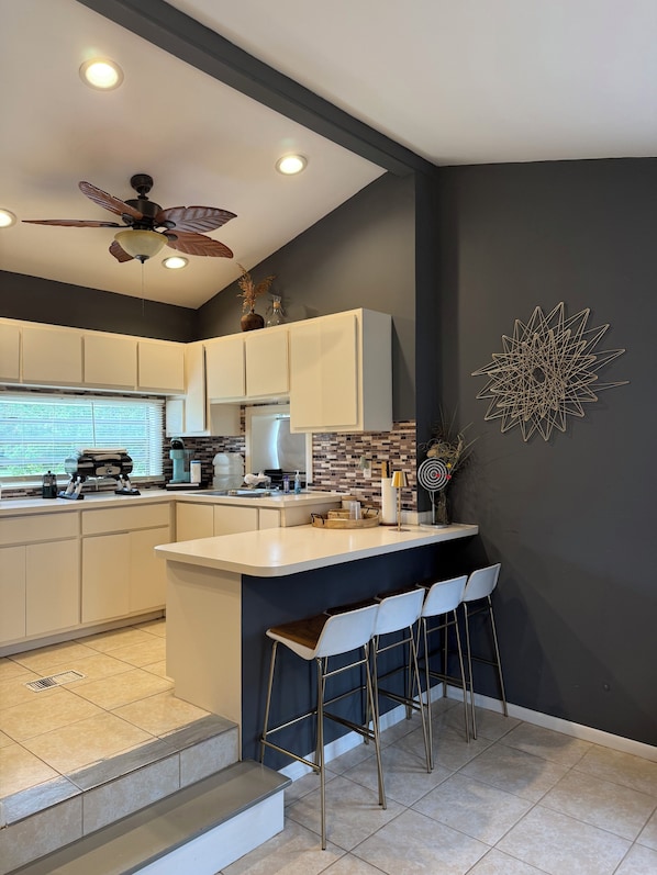 A modern kitchen with a central island, bar stools, and a ceiling fan.