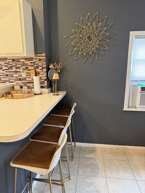 A kitchen with a curved countertop, a decorative wall piece, and a window with blinds.