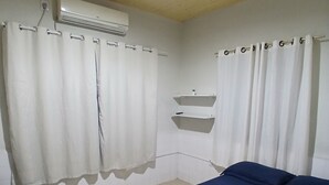 A bedroom with a bed, a suitcase, a wall-mounted air conditioner, and a tiled floor.