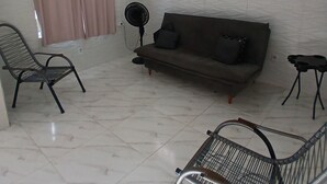 A room with a white ceiling, a sofa, a chair, a standing fan, and a small table.