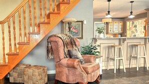 Een woonkamer met een houten trap, een bar en een grote fauteuil met een plaids.