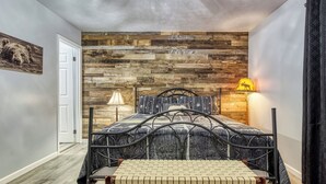 Un dormitorio con cama, un banco, pared de madera, lámpara y una puerta.